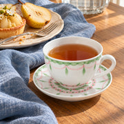 AI-assisted concept image of the botanical cup and saucer with pastries and blue linen; props are not included.